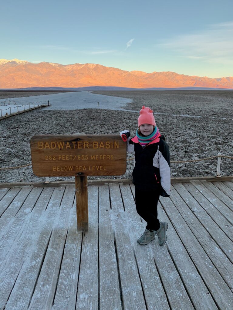 Cameron at sunrise at the Bad Water Basin Sign in Death Valley National Park. The mountains in the background are just getting the first light of day.