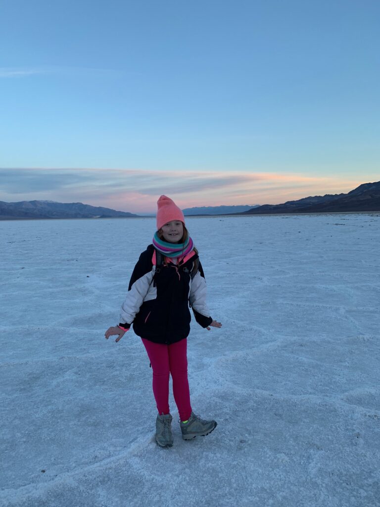 Cameron standing on the salt flats in the middle of Death Valley National Park. In the winter wearing hat, gloves and jacket. Sunrise is just starting and there is color in the sky.