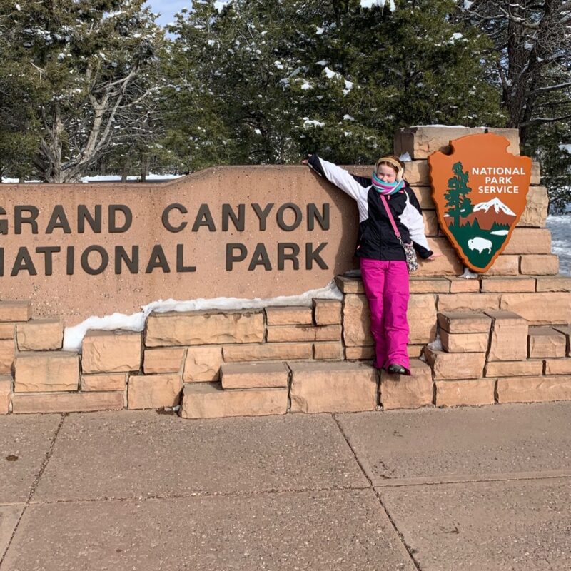 Cameron in front of teh Grand Canyon National Park sign.