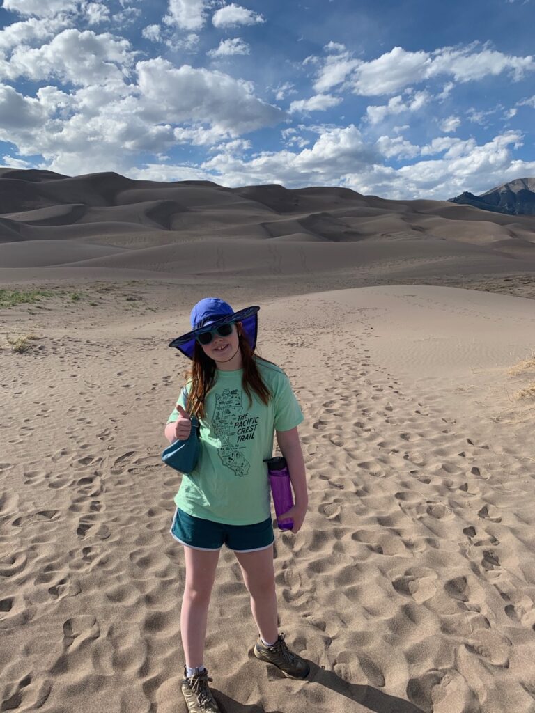 Cameron getting ready to hike to the top of the dunes with me, lots of footprints in the sand and blue sky with dotted clouds. 