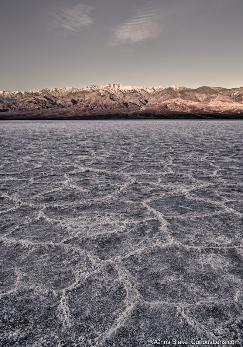 Photo of Death Valley National Park, the hottest, driest, and lowest point in the U.S. with expansive salt flats leading to mountain ranges in the background. Captured in the late blue hour during winter 2019.