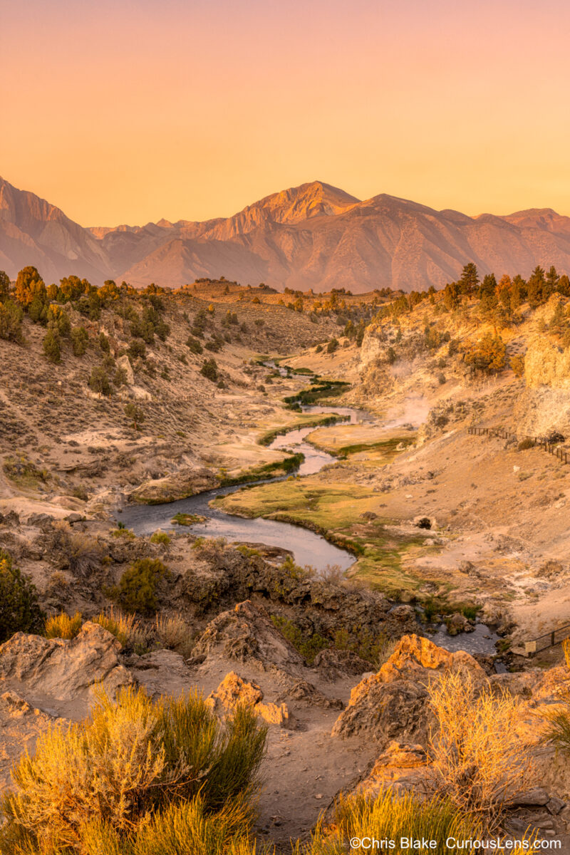 Brees Lookout, a natural hot spring in Mammoth Lakes, California, with steam rising from the lava beneath a winding river. At sunrise, the Sierra Nevada mountains glowed with a vibrant yellow and red sky, partly due to the 2021 California wildfires.