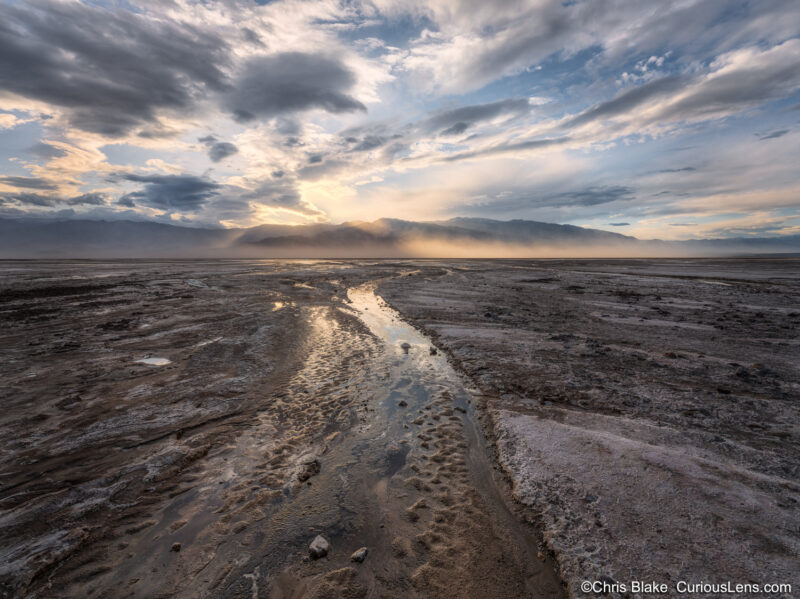 A creek had formed in Death Valley from the recent rain. The photo shows the creek leading into the mountains with dotted light breaking through the clouds.