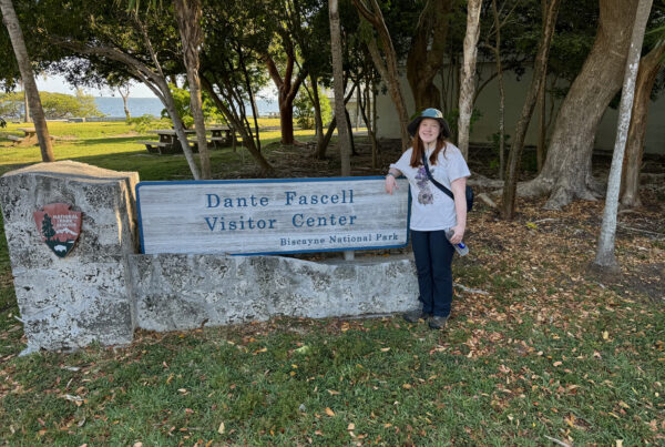 Cameron standing in front of the sign for Dante Fascell Visitors Center in Biscayne National Park. She is wearing a hat and has a huge smile on her face.