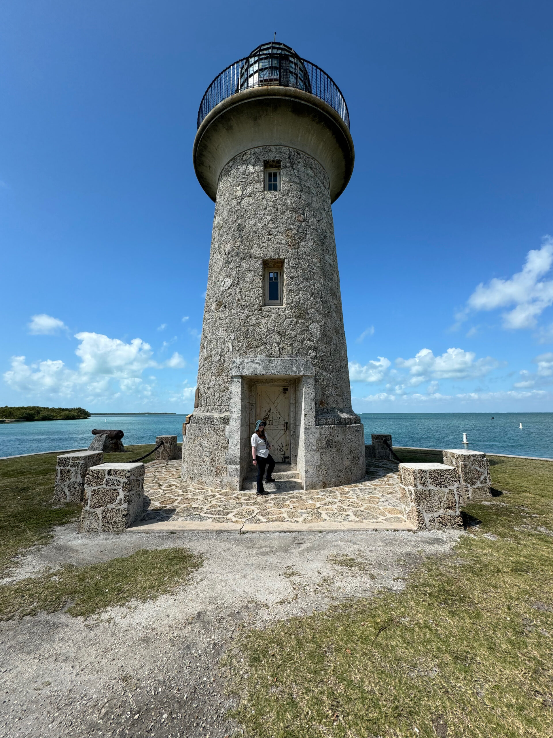 Cameron standing in the doorway of the lighthouse on Boca Chita Key. Blue sky, some puffy clouds and the ocean are in the background.