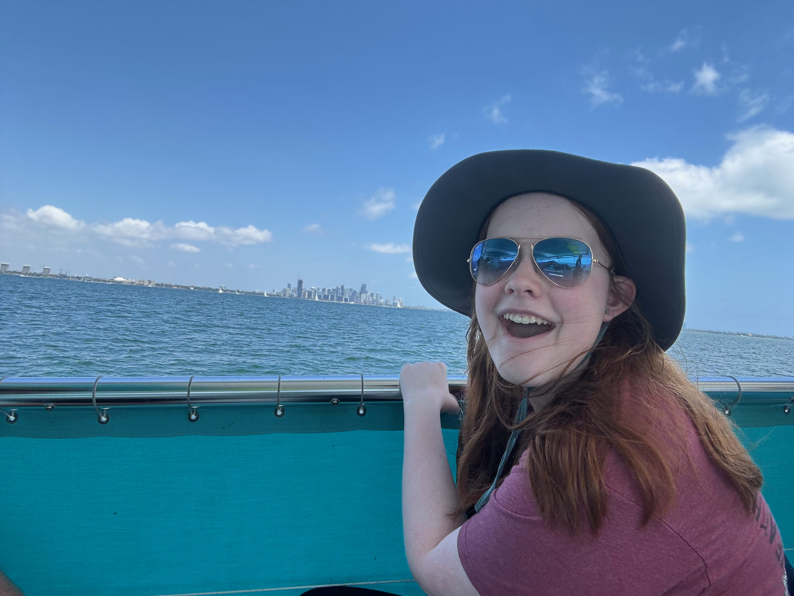 Cameron wearing a hat and sunglasses has a big smile as she checks out the Miami skyline from our Boat tour.