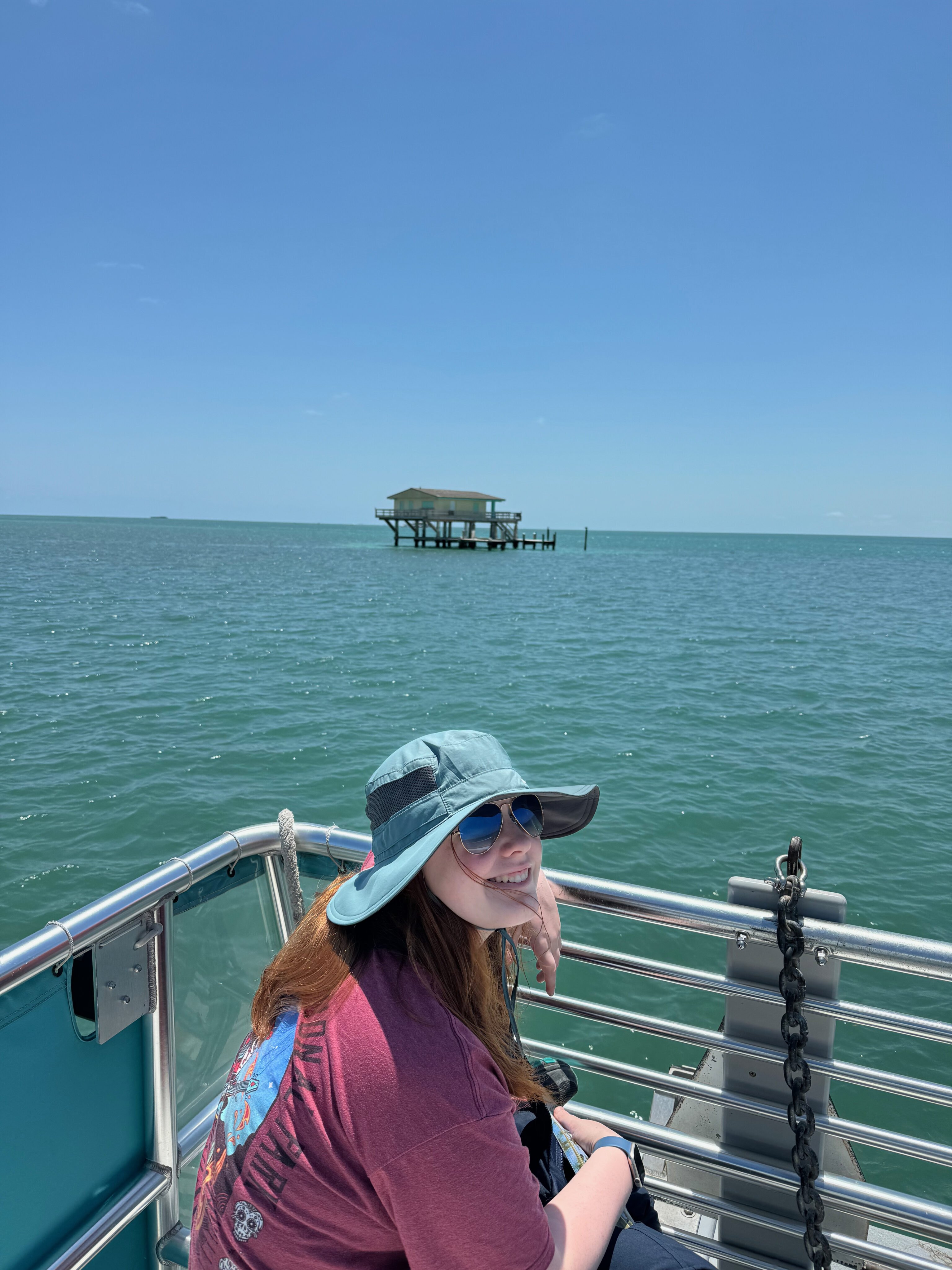 Cameron sitting at the edge of the boat while we tour Stiltsville, and one of the houses can be seen in the distance.