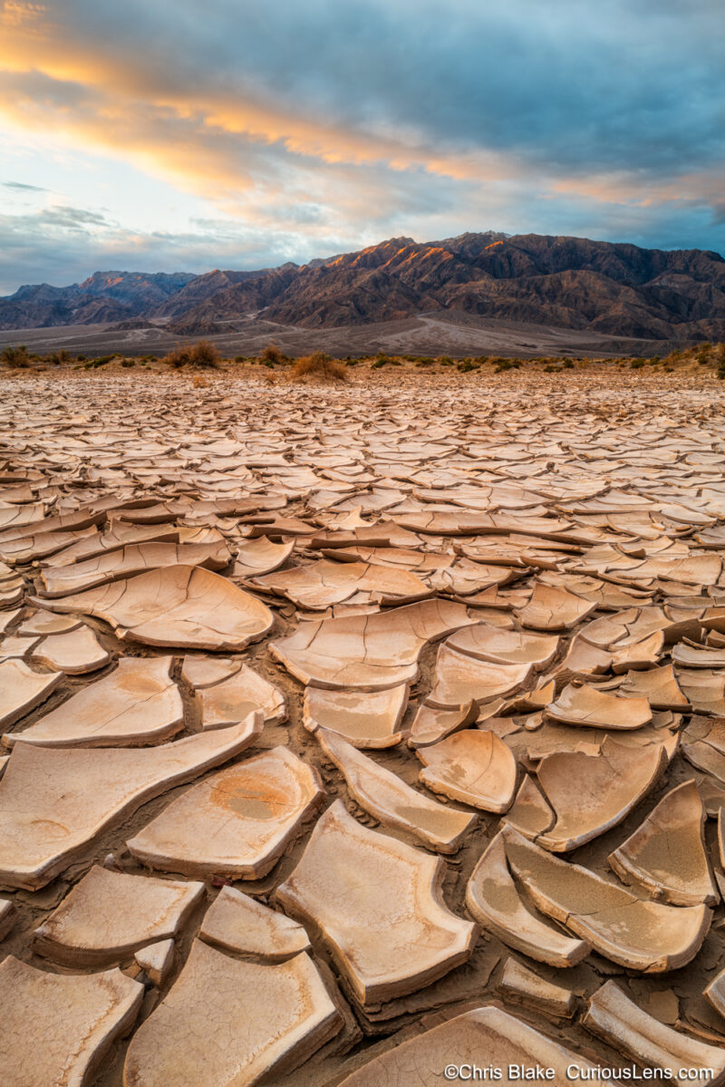 Death Valley with dried cracked mud in the foreground and the mountain range in the back. Taken just after sunset with the cloud alive with color.