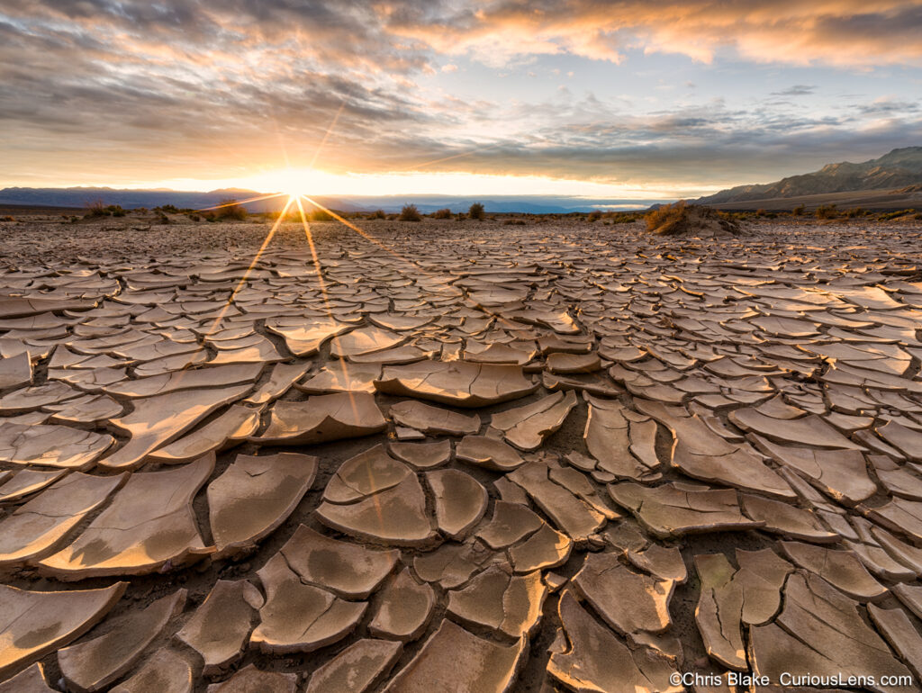 Sunrise in Death Valley National Park California. Cracked mud in the foreground, a sun star and colorful clouds.