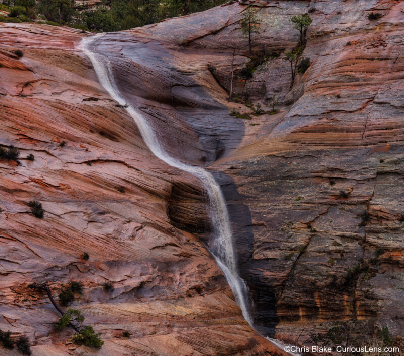 Zion National Park in February 2024: Experience the unusual warmth and rainfall creating new waterfalls cascading down majestic sandstone formations. This multi-row panorama, crafted from 16 images, captures the rush of water against vibrant red sandstone, beautifully illuminated by reflected light.