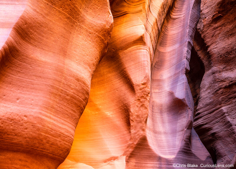 A stunning view inside Antelope Canyon, located near Page, Arizona, showcasing the intricate rock formations of a slot canyon. The image captures a point in the canyon where a narrow opening allows sunlight to cascade through, illuminating the sandstone walls. The light creates a striking contrast with the dark purple hues in the center of the frame, where erosion has shaped the rock into a smooth, slide-like formation. This vibrant scene highlights the diverse textures and contours carved by wind and water over millions of years, demonstrating the unique and captivating beauty of this renowned natural wonder.