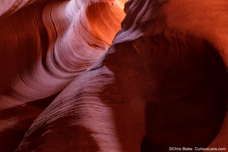 Antelope Canyon, near Page, Arizona, is a renowned slot canyon shaped by water and wind over millions of years. This photo shows a dark chamber deep within the canyon, where a narrow opening above allows a small stream of light to filter in, creating a stunning gradient from bright yellow to deep red. The image captures the intricate sandstone textures with a multi-exposure technique to enhance focus and dynamic range.