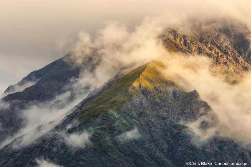 Bonanza Mountain in Wrangell-St. Elias National Park near Kennecott. Early morning light illuminates the mountain's right flank with wispy clouds and glowing grass and shrubs.