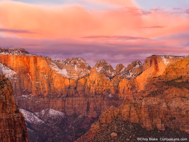 Experience the breathtaking beauty of Zion National Park's Canyon Overlook trail at sunrise. While the pre-dawn ascent may be shrouded in darkness, the journey back reveals stunning vistas of Pine Creek and the vast canyon landscape. The trail's end provides a panoramic view dominated by the Tower of the Virgin, a towering sandstone monolith among Zion Canyon's western peaks. Surrounding the Tower of the Virgin, other iconic formations such as The Sundial, The Witch Head, Broken Tooth, Rotten Tooth, Altar of Sacrifice, Bee Hive, and The Sentinel stand majestically against the early morning sky. This scene, with its snow-capped peaks and unique silhouettes, captures the essence of Zion's timeless allure. This image not only showcases nature's grandeur but also reflects a serene moment of beauty that resonates with all who visit.