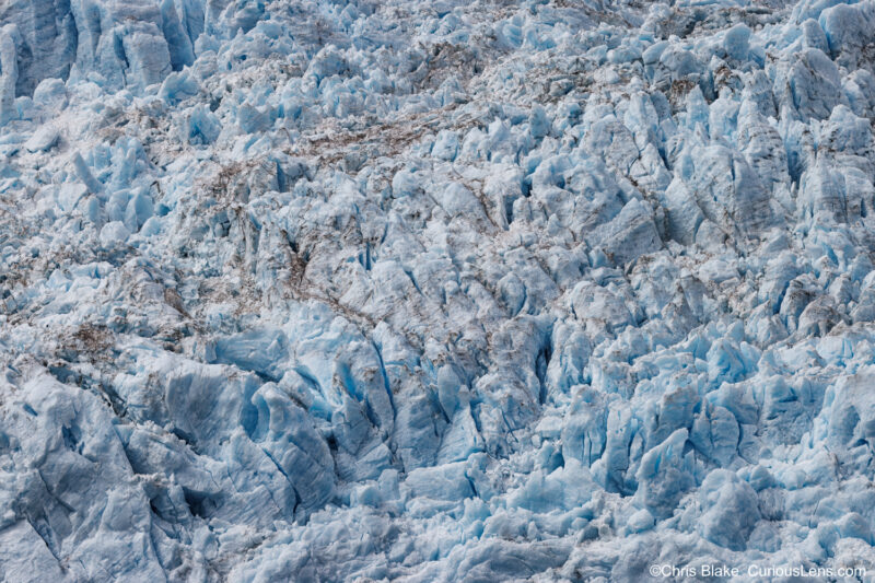 Close-up of a glacier with intricate ice details, deep veins, and mesmerizing blue water in a tranquil bay.