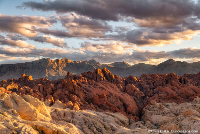 A stunning sunset in Nevada's Valley of Fire. Warm light bathes the layered rock formations, casting rich golden hues across the landscape. Dramatic clouds frame the scene, adding depth and contrast. A breathtaking view captured just before sunset.