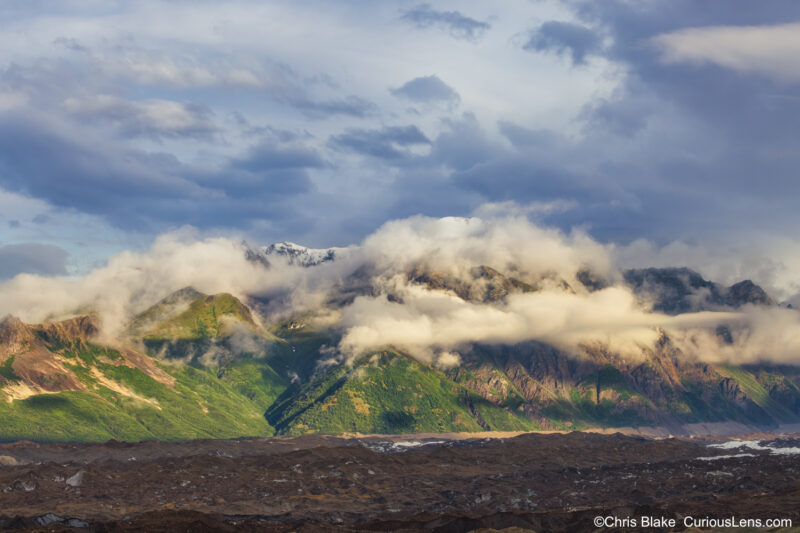 Fireweed Mountain in Wrangell-St. Elias National Park. View from Kennicott with glaciers, rivers, green hills, and snow-capped peaks. Sunrise with low-lying clouds and dramatic storm clouds.