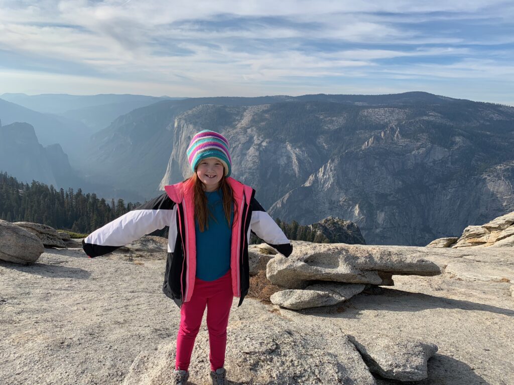 Cameron standing on top of Glacier Point in Yosemite National Park at sunset with a sky full of clouds.