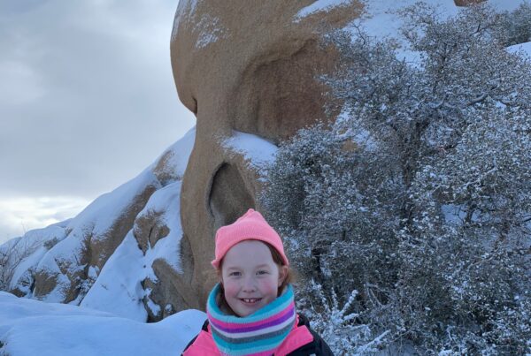 Cami in front of Skull Rock in the snow in Joshua Tree National Park.