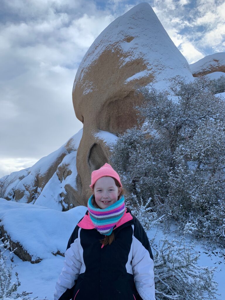 Cami in front of Skull Rock in the snow in Joshua Tree National Park.