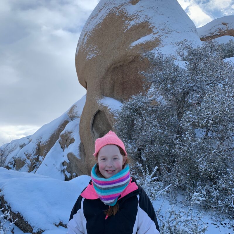 Cami in front of Skull Rock in the snow in Joshua Tree National Park.