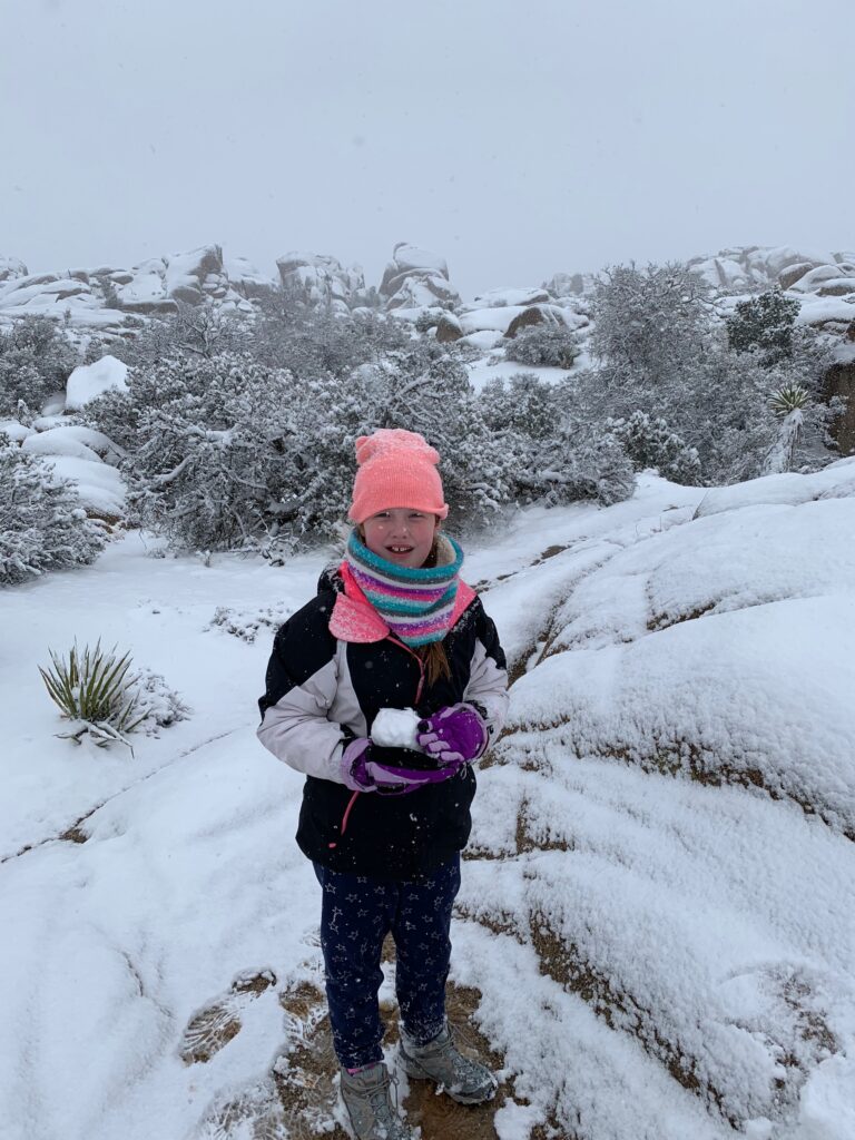 Cami making a snowball at Skull Rock, in the snow in Joshua Tree National Park.