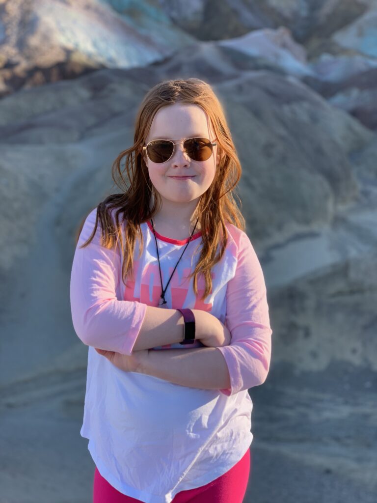 Cameron standing in Death Valley at Artists Palette, with her arms crossed wearing sunglasses.