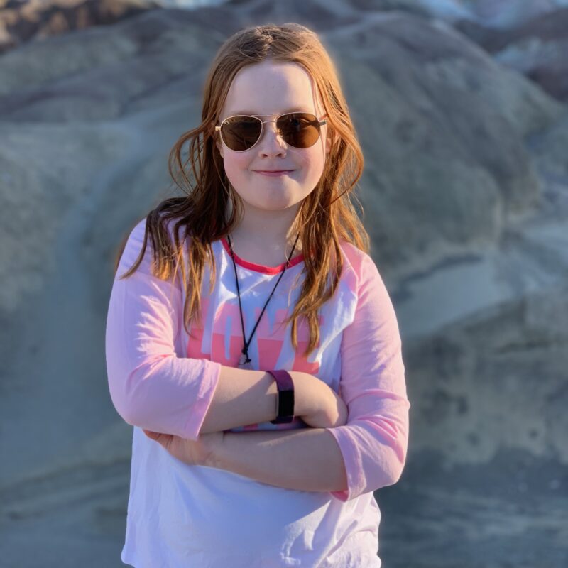 Cameron standing in Death Valley at Artists Palette, with her arms crossed wearing sunglasses.