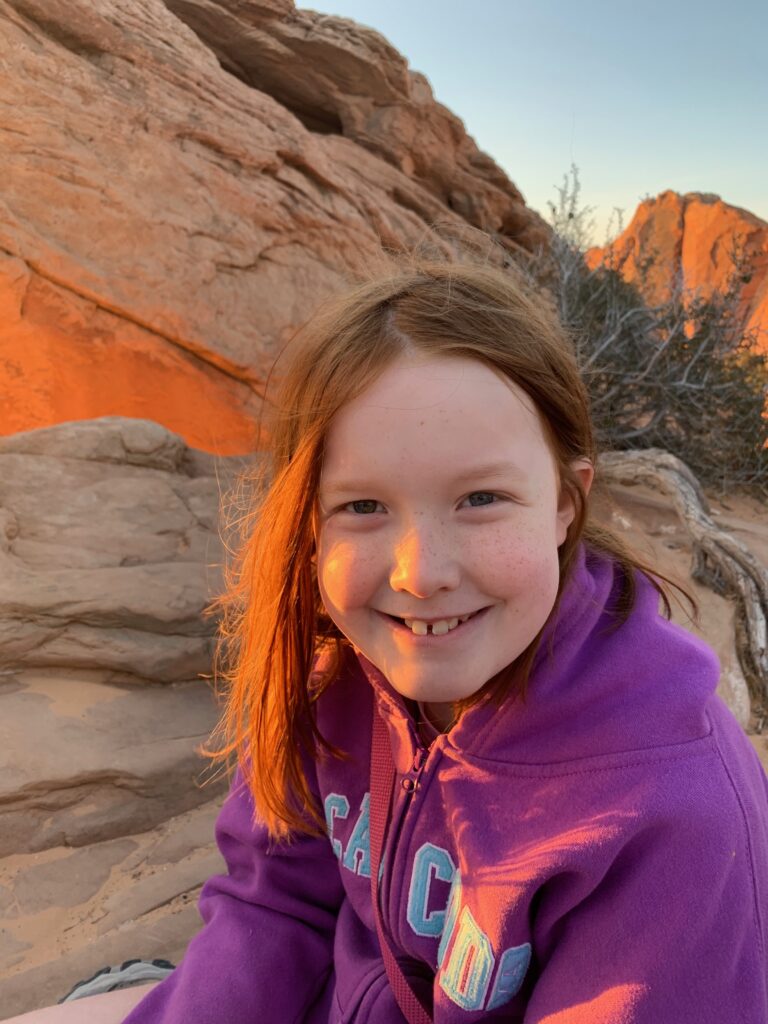 Cameron sitting at Mesa Arch at sunrise, with the warm red light washing across her face.