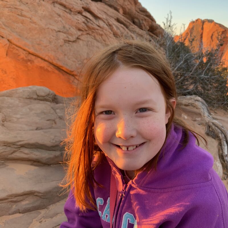 Cameron sitting at Mesa Arch at sunrise, with the warm red light washing across her face.