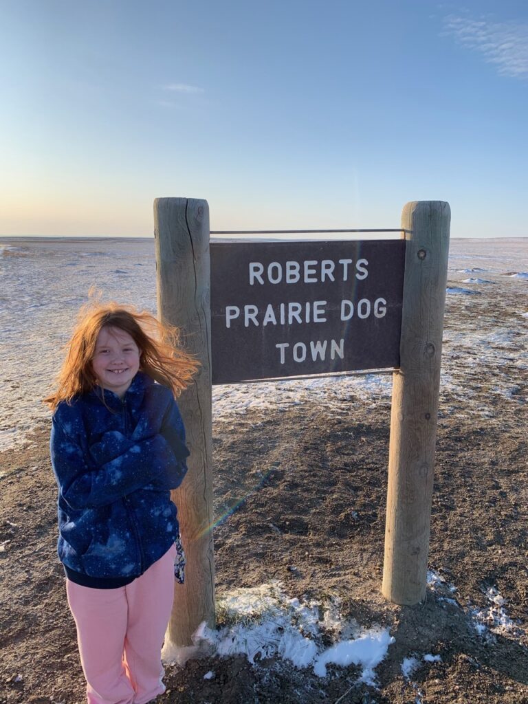 Cameron on a windy day standing in front of the Roberts Prairie Dog Town sign in Badlands National Park.