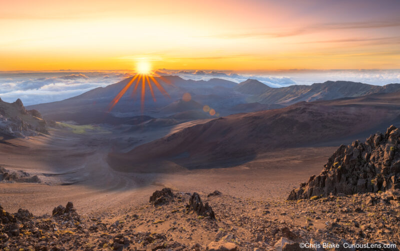 Summit of East Maui Volcano at Haleakalā, where sunrise illuminates cinder-cone volcanoes. Captured from above the clouds at over 10,000 feet on an August morning.