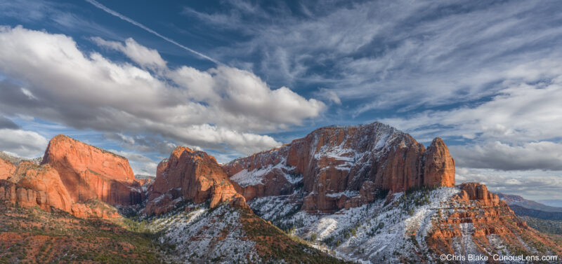 Scenic view of Kolob Canyons in Zion National Park during a winter afternoon. The scene features dramatic red sandstone cliffs, illuminated by a low sun, with patches of white snow and a dark blue sky overhead. The unique geology of this area, located in the northwest corner of Zion, creates a stunning landscape with narrow parallel box canyons and towering 2,000-foot-high cliff walls. This tranquil setting captures the essence of a peaceful escape in a southwestern landscape, offering breathtaking vistas and serene hiking trails.