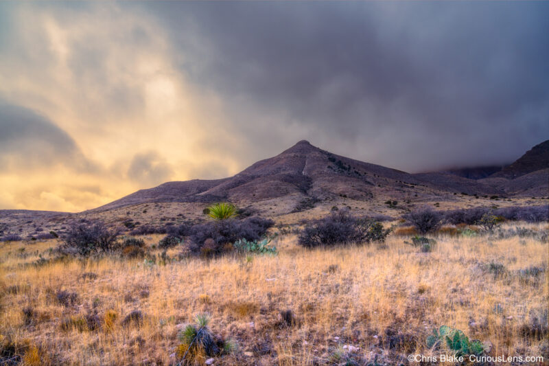 Guadalupe Mountains National Park in western Texas, near the New Mexico border, features diverse landscapes including salt-white dunes, expansive grasslands, and towering mountains. During a stormy evening, high winds blew across a scenic high-desert grassland, where sunlight pierced through clouds, casting deep contrasts. In the distance, the peaks, including Texas's highest point, Guadalupe Peak at 8,751 feet, were enveloped by low-flying clouds.