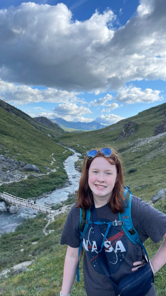 Cameron posing and smiling for a photo on top of small mountain and the savage river and its bridge is below us.