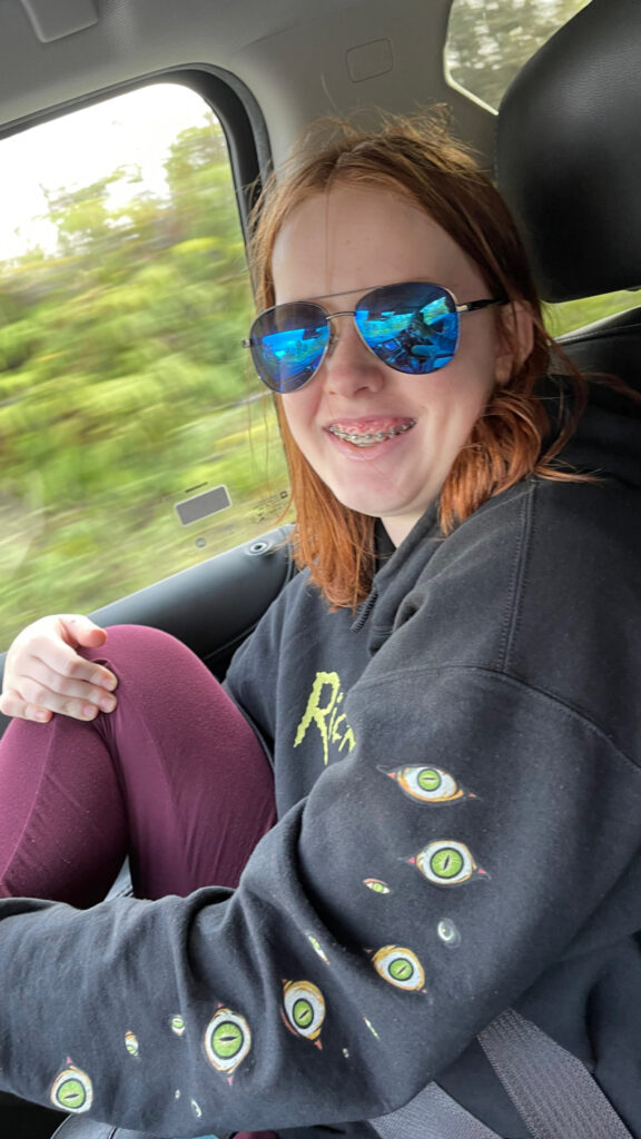 Cameron sitting in the moving car, with a big smile on her face, wearing aviator sunglasses as the scenery passes by on the Chain of the Craters Rd in Volcanos National Park.