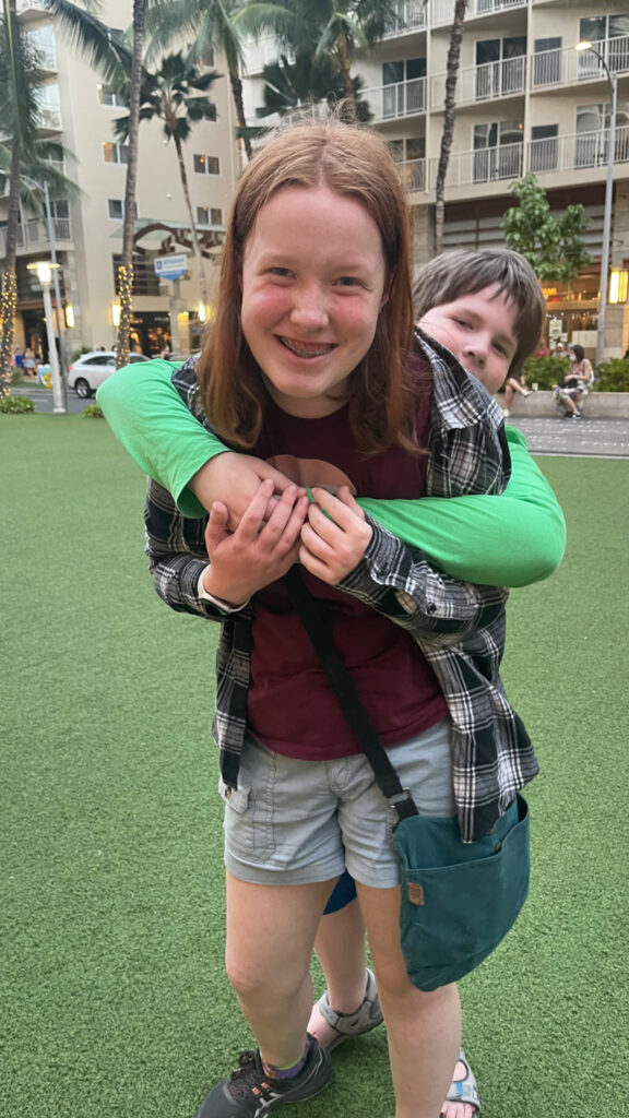 Collin giving Cameron a huge from the back, outside in a park in Waikiki.