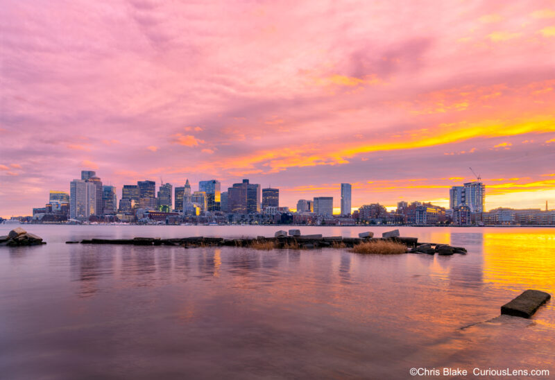 East Boston sunset with vibrant sky, clear view of downtown Boston, Custom House, Long Wharf, and no boat traffic.