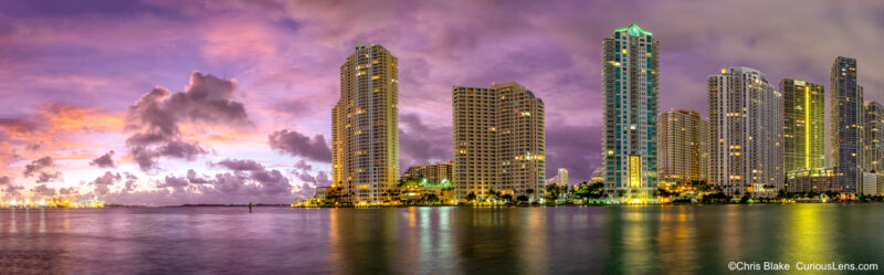 Sunrise over Brickell Key with vibrant red and purple sky, building lights, and reflections in the water, Miami, Florida.