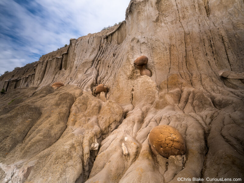 Cannonball Concretions in Theodore Roosevelt National Park's North Unit with wet sandstone wall, spherical rock formations, and clearing sky after rain.