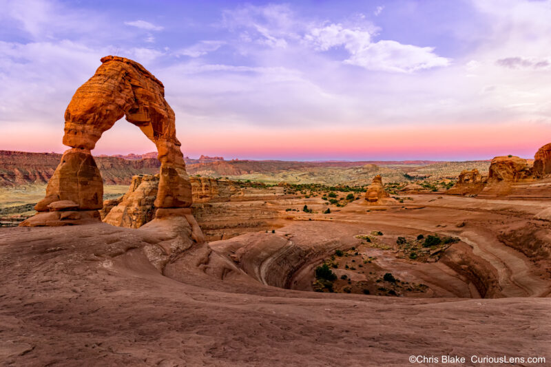 Delicate Arch at sunrise in Arches National Park with soft lighting, horizon color, and grand scale of 45ft high and 32ft wide."