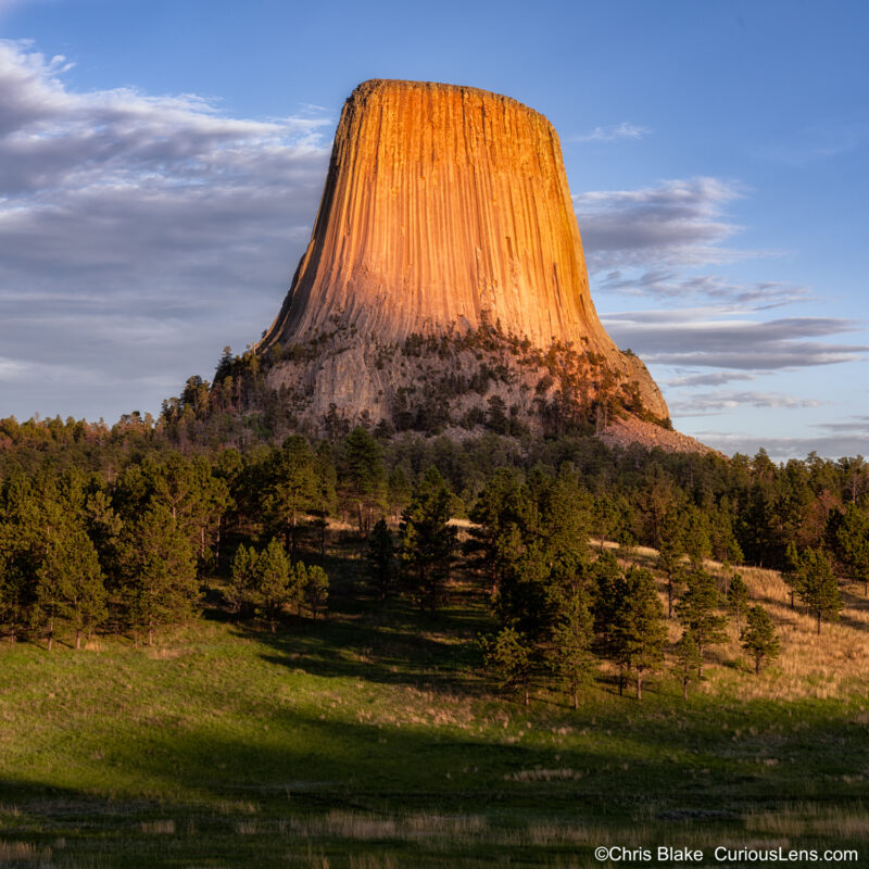 Sunset at Devils Tower with rolling grass field, trees, and time composite blending golden light and blue hour.