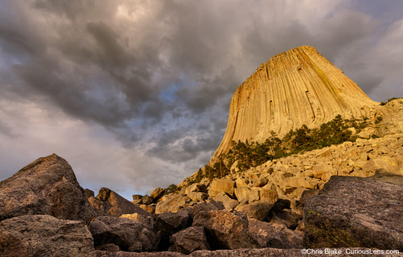 Devils Tower in Wyoming with last sunlight hitting the face, clouds breaking apart, and afternoon thunderstorms.