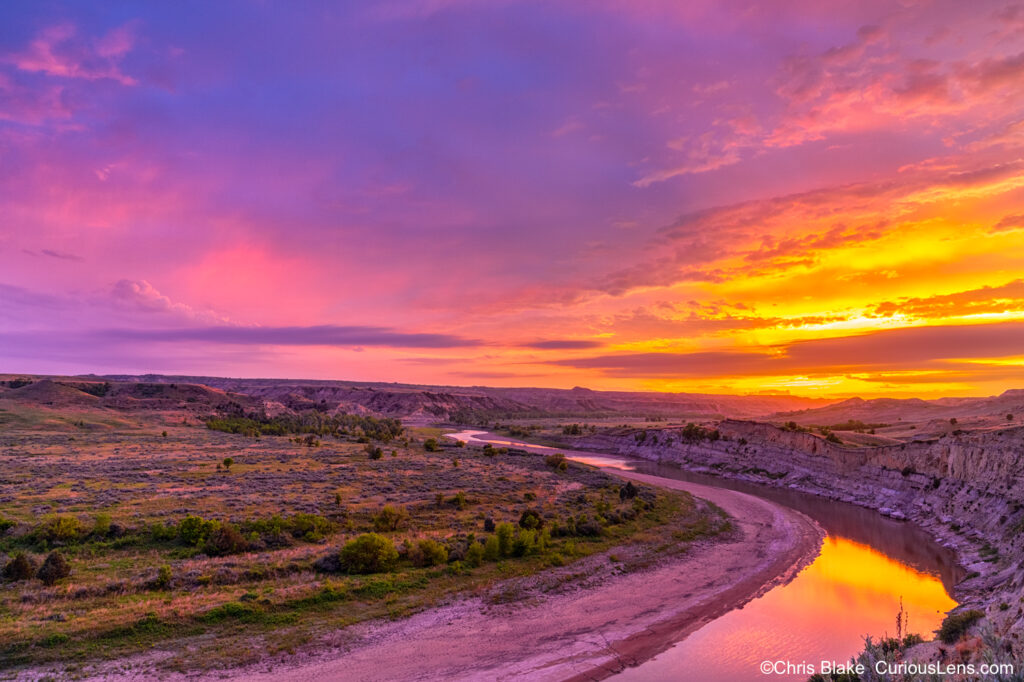 Sunset over Little Missouri River with bright red to purple sky reflecting in the river and grassland.