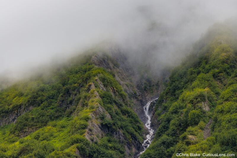 Exit Glacier in Kenai Fjords National Park with accessible public roads, picturesque valley, meandering river, mountain peaks, clouds, and vibrant green foliage.