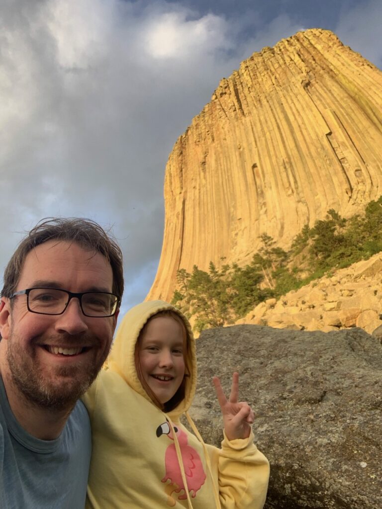 Cameron and myself at sunset hiking the Tower Trail and the Devils Tower, at sunset with warm yellow light on the rock face.