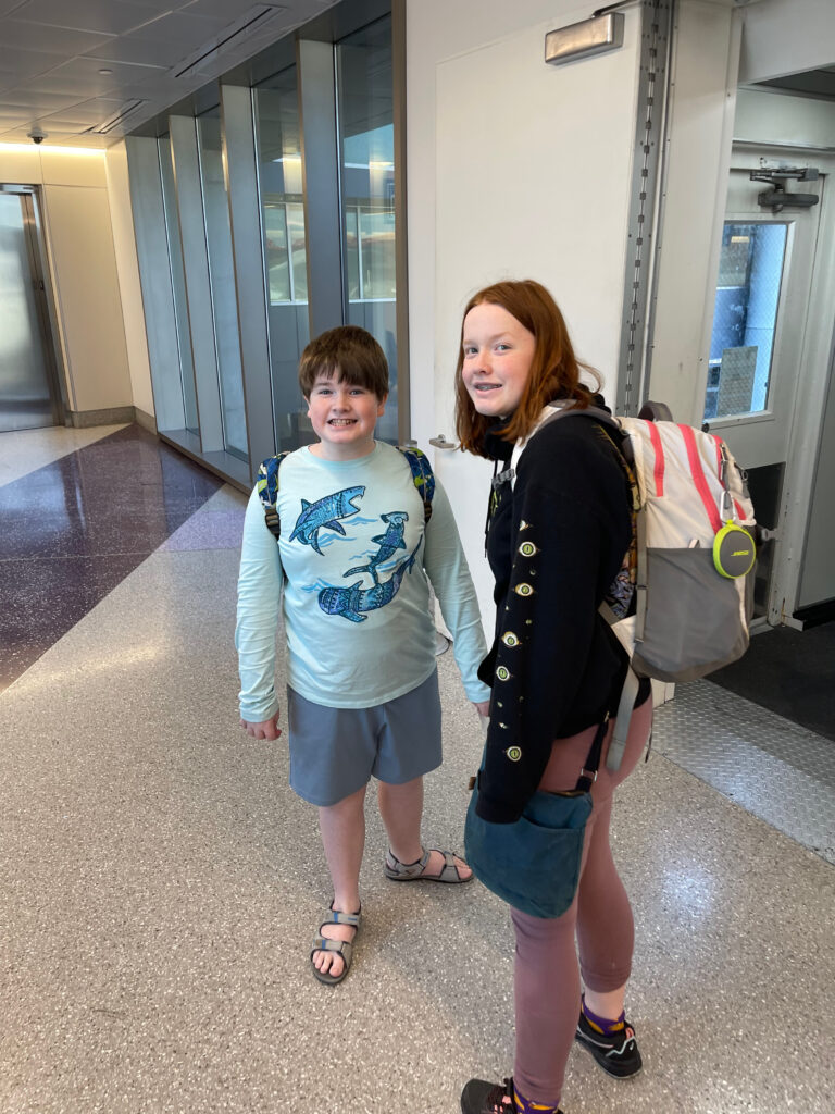 Cameron and Collin about to board an airplane - both with backpacks on at Boston Logan airport.