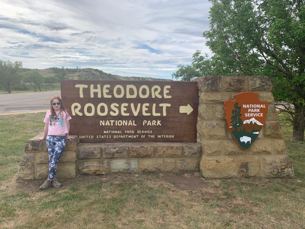 Cameron standing in front of the Theodore Roosevelt National Park sign.