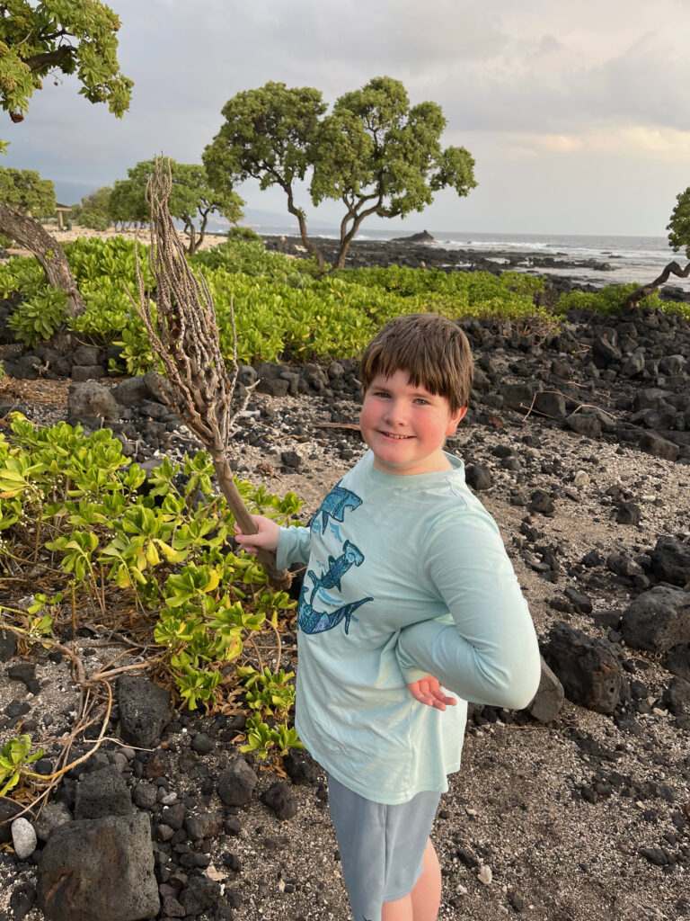 Collin holding a branch on Old Kona Airport Beach, with lava rock and sand all around him.