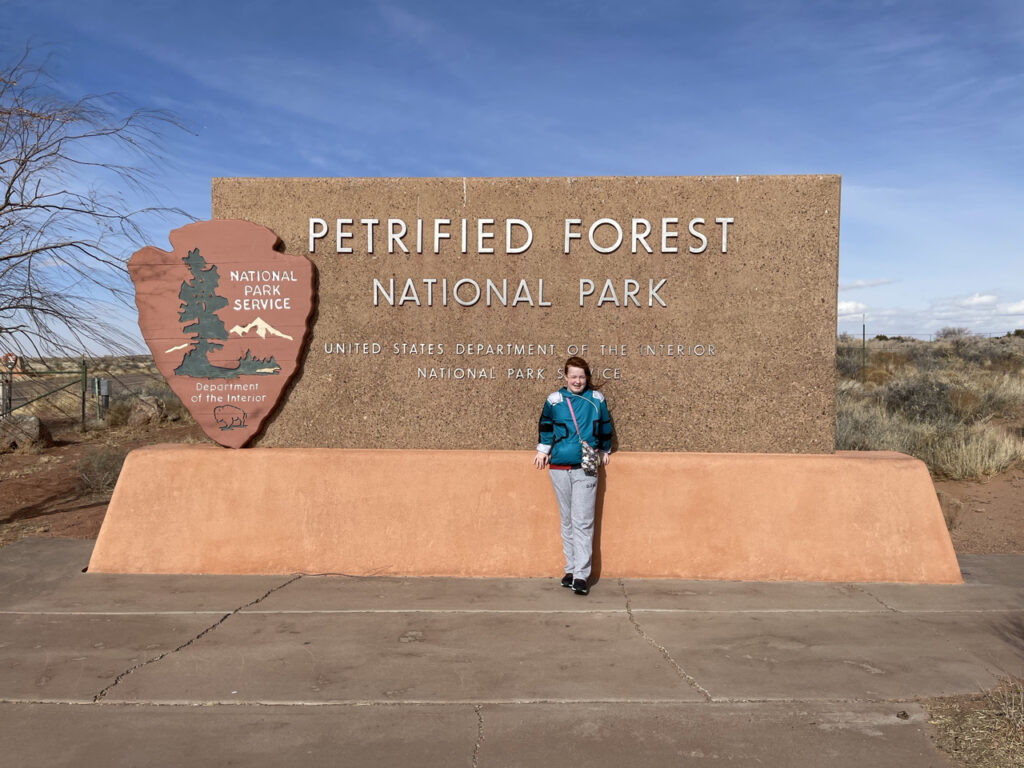 Cameron standing in front of the Petrified Forest National Park sign. 